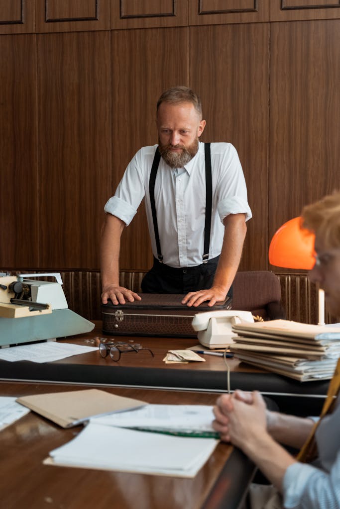 A professional man in a vintage office setting reviewing documents with a colleague.
