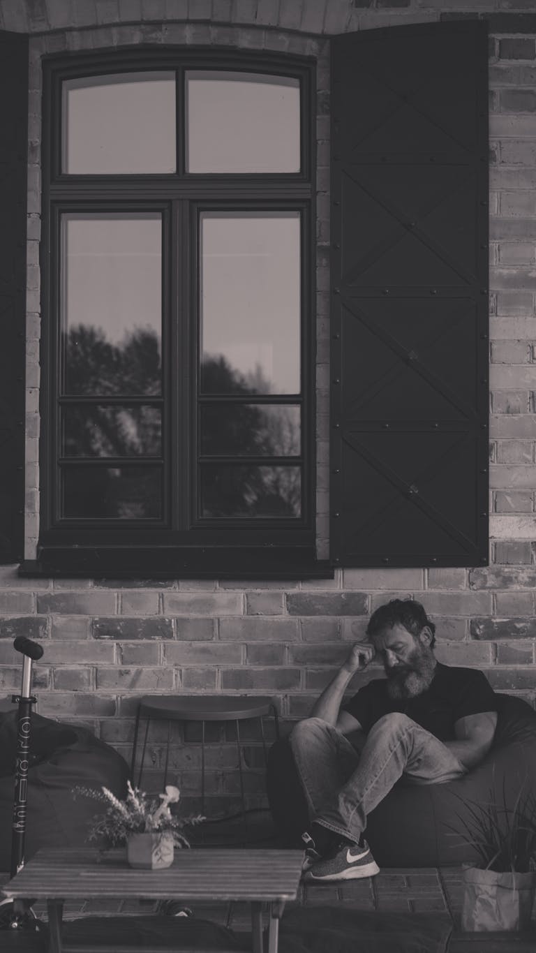 Black and white photo of a man sitting by a window, reflecting a calm, moody atmosphere.