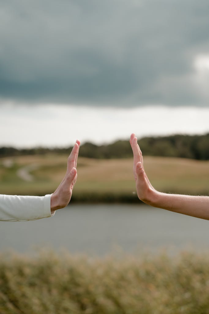 Hands reaching out under cloudy skies above a peaceful rural meadow.